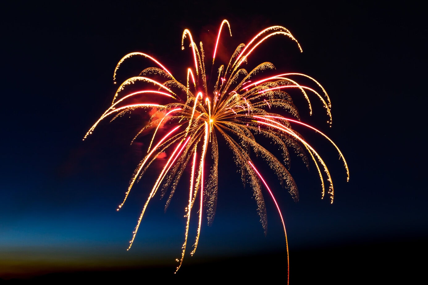 Fireworks resembling a golden waterfall drape gracefully above the dark horizon during a nighttime celebration.