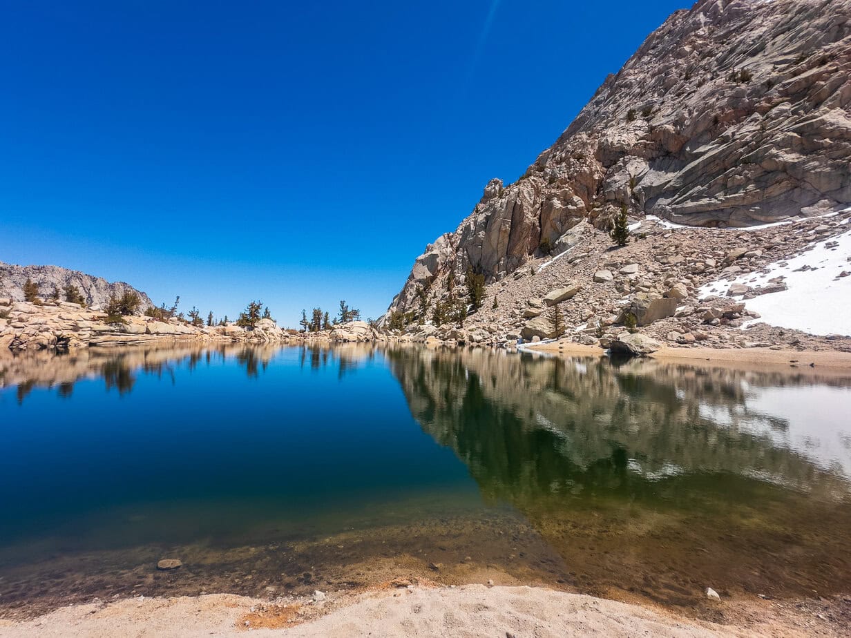 Crystal-clear waters of Lone Pine Lake reflecting granite cliffs and a bright blue sky along the trail in California’s Eastern Sierra.