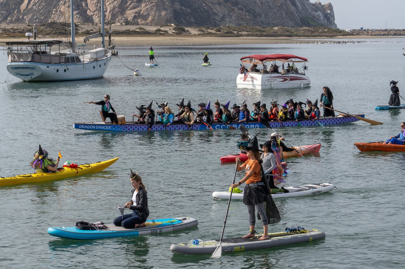 Costumed paddlers and a group boat participating in the Morro Bay Witches Paddle near Morro Rock
