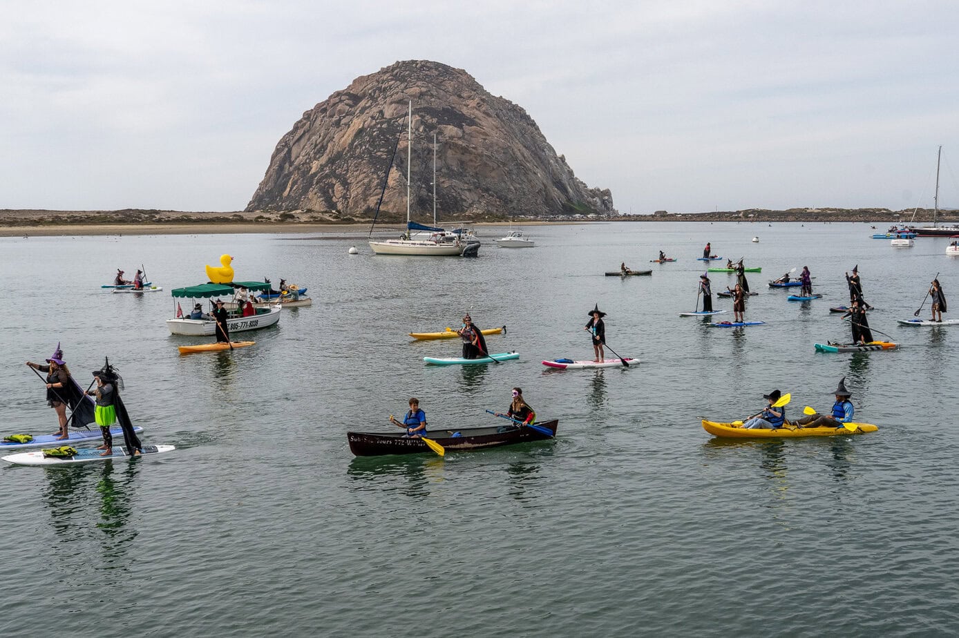 Costumed paddlers crossing Morro Bay with Morro Rock in the background during the Witches Paddle