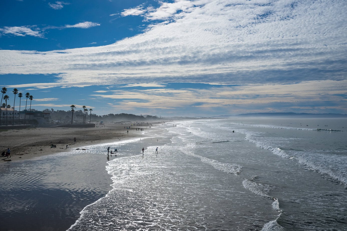 Wide sandy shoreline at Pismo Beach with waves, morning light, and people walking along the coast