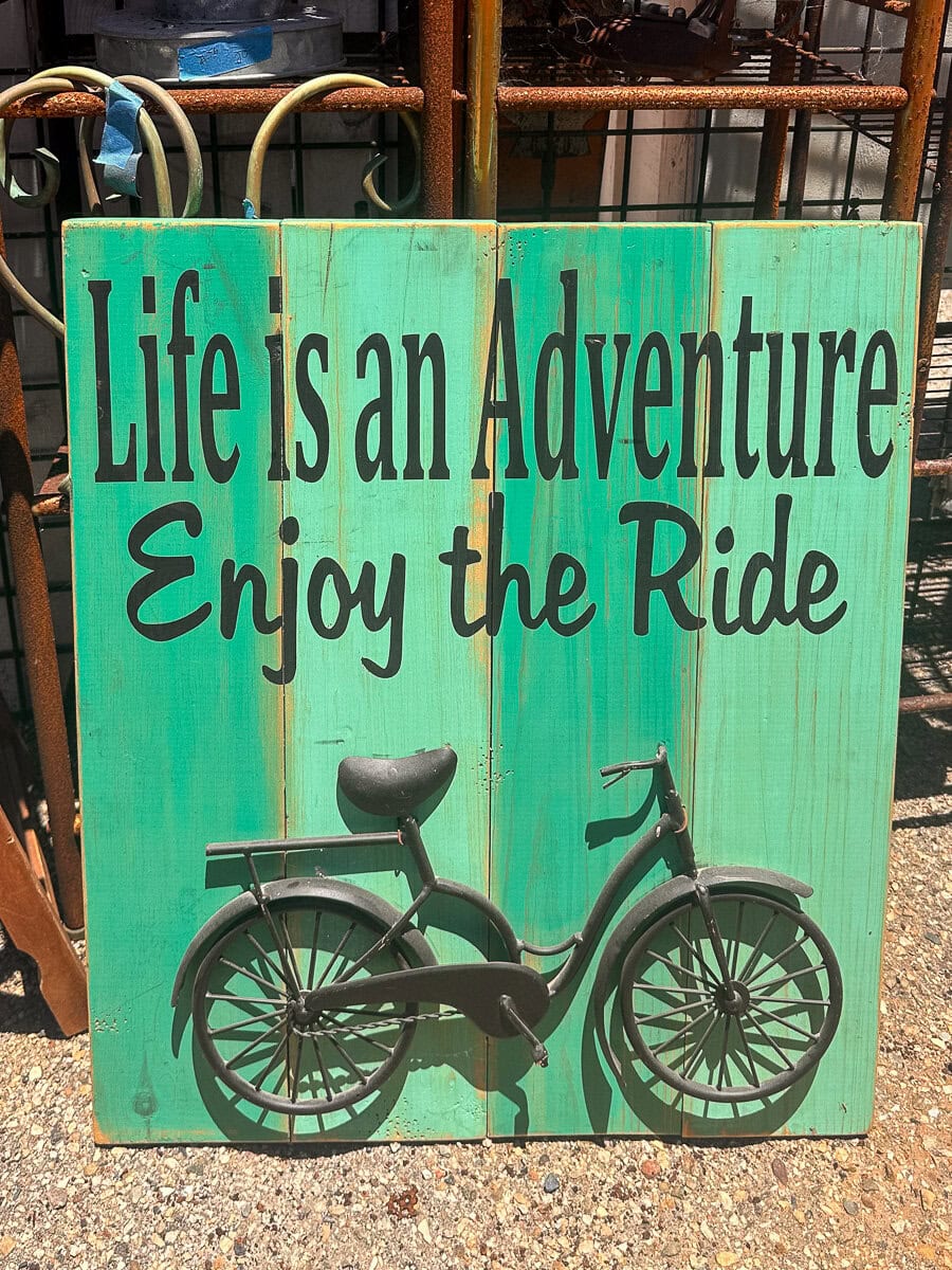 Colorful Cayucos wooden panel reading Life is an Adventure Enjoy the Ride with a bicycle illustration.