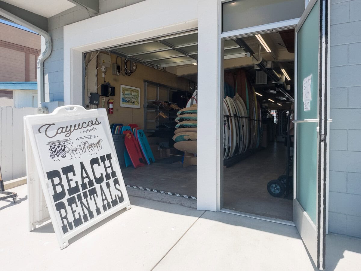 Surfboard rental sign and beach gear outside a surf shop in Cayucos.