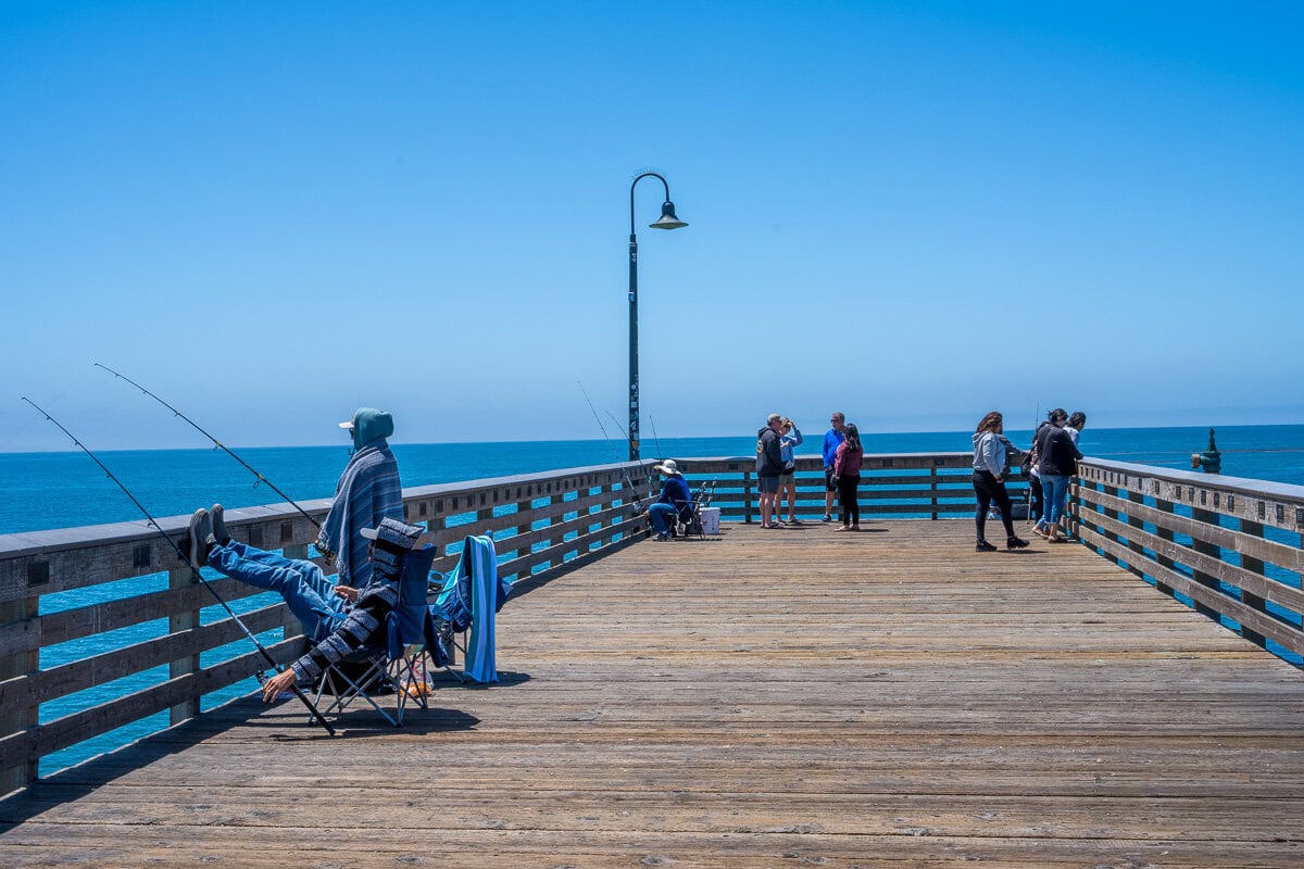 People fishing from the end of the wooden pier beneath a clear blue sky