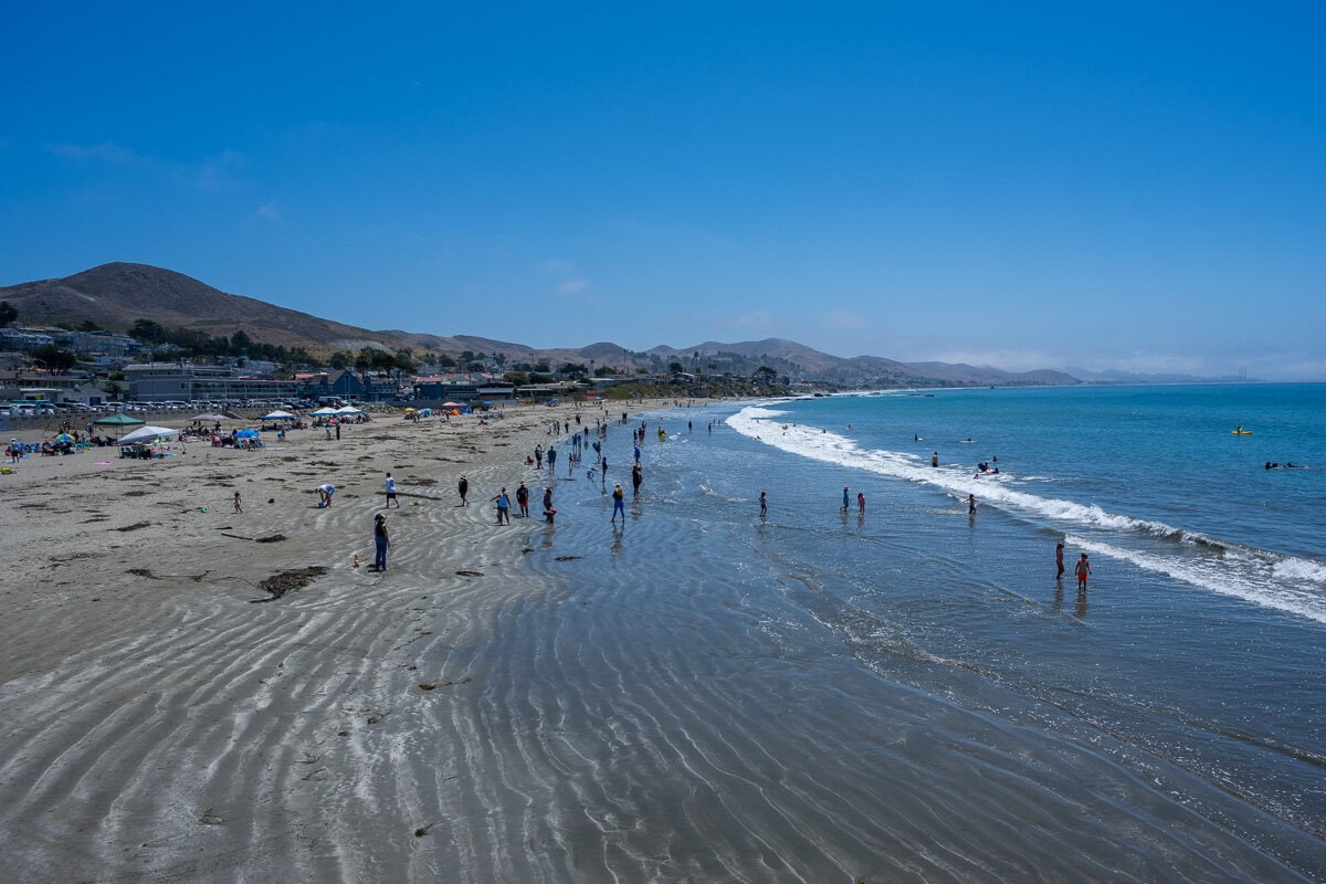 Wide view of Cayucos Beach, shallow surf, and people walking along the shoreline