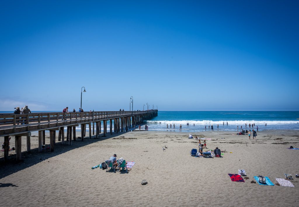 The wooden pier stretching over a sandy beach dotted with visitors on a sunny day