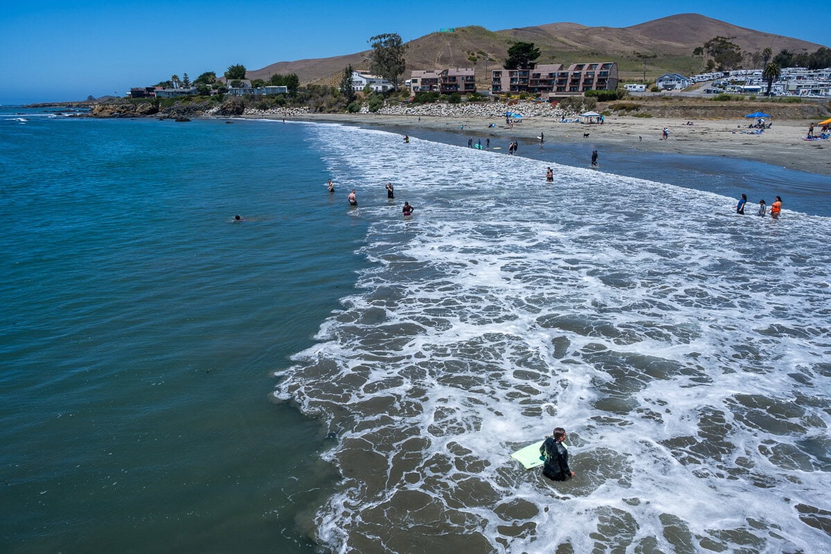 Elevated view from Cayucos Pier of waves curling toward the beach and waterfront homes