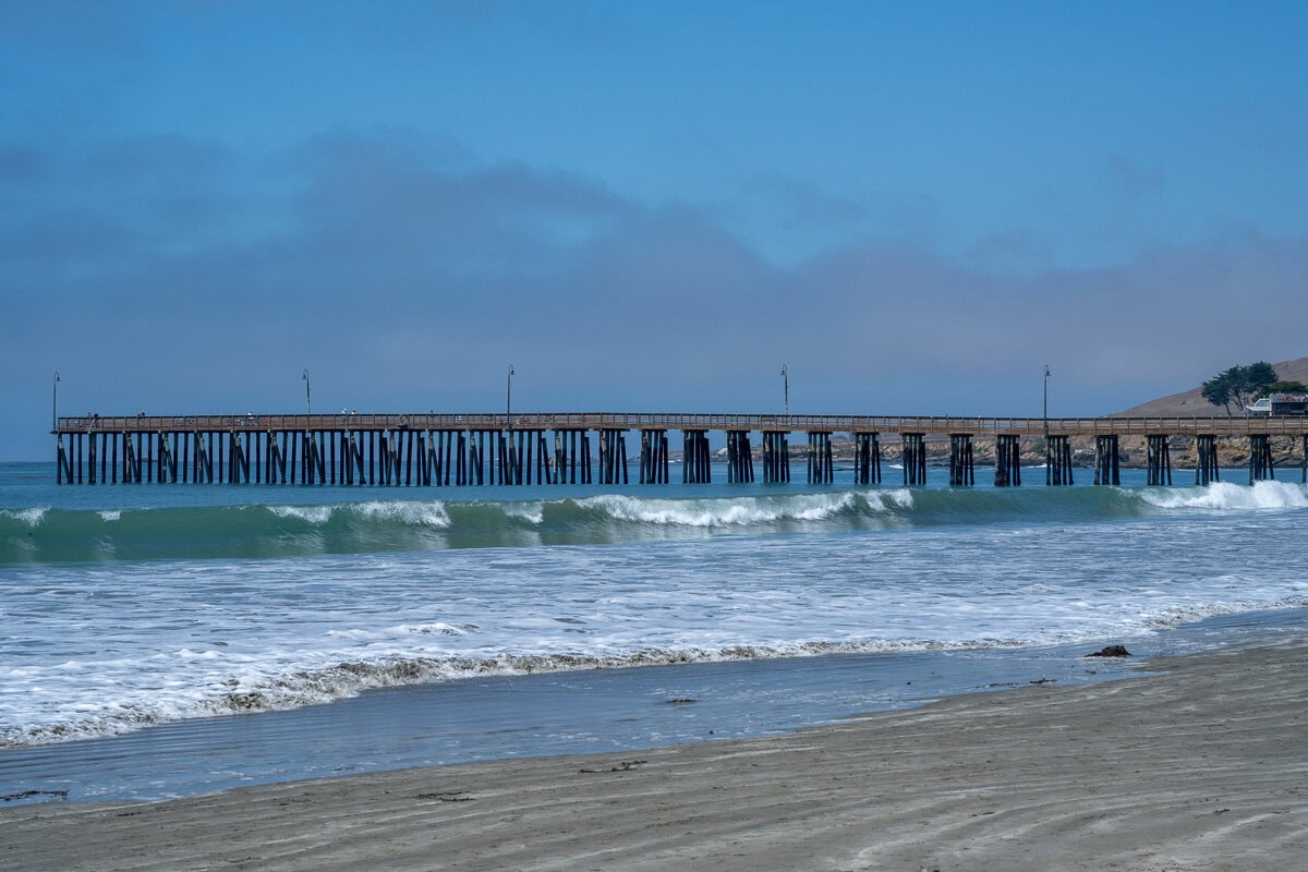 Ocean waves rolling toward Cayucos Pier under a low bank of coastal fog