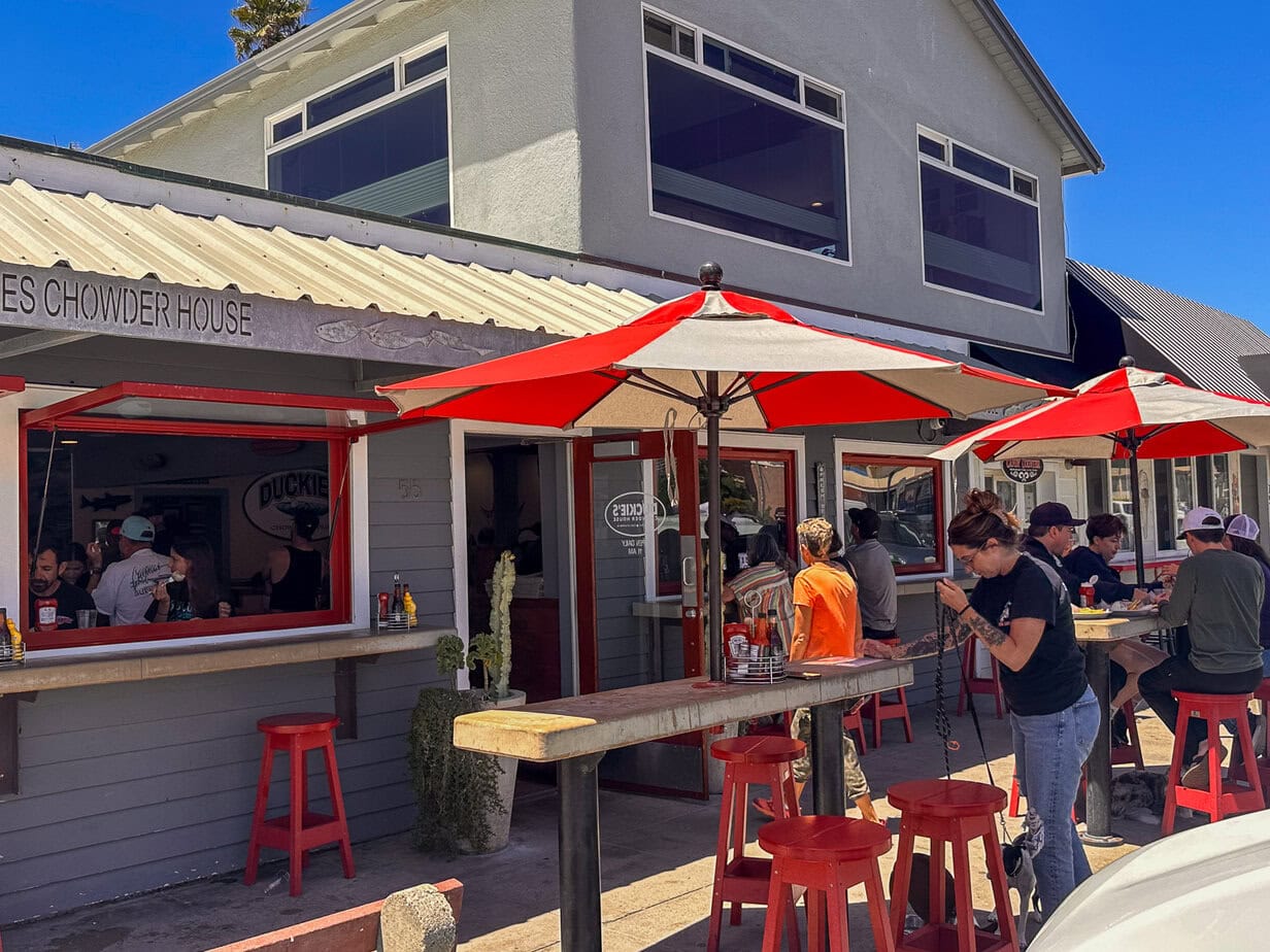 Outdoor seating and red umbrellas outside Duckie’s Chowder House near Cayucos Pier.